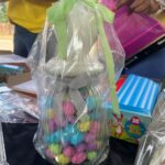 Clear gift bag filled with colorful candy eggs, tied with a green ribbon, resting on a table.