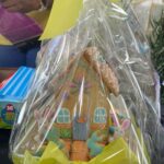 Decorated gingerbread house cookies inside a clear gift bag with a yellow ribbon, ready for gifting.