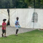Two young boys walk along a gravel path beside a large white tent with a rounded window in a park.