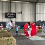 Indoor kids’ play area with hay bales, a red plastic play structure, and children exploring on colorful mats with an adult supervising.