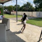 Two kids running on a sunny patio next to white seating, with a grassy yard and string lights overhead at an outdoor event.