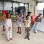 Group of kids in a covered play area holding gift bags at a community event.